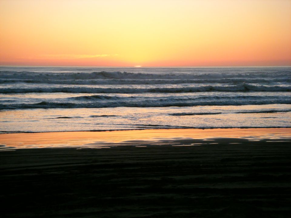 Sunset over the ocean with waves and wet sand.