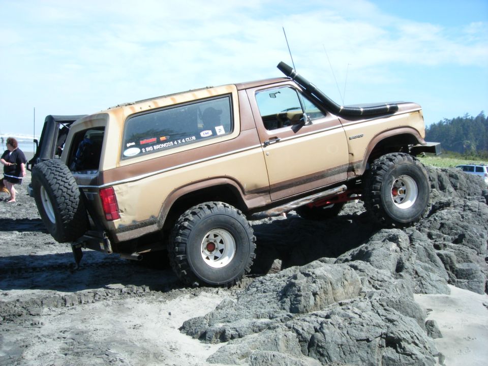 Lifted brown and tan Ford Bronco on a rocky beach with snorkel.