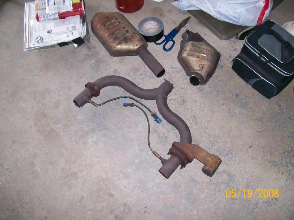 Rusty exhaust Y-pipe and two removed catalytic converters on garage floor