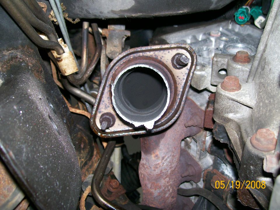 Close-up of a rusted exhaust manifold connection on a vehicle engine.