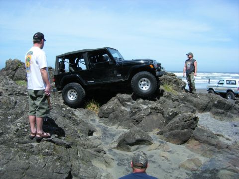 1994 Ford Explorer - Jeep Wrangler navigating a rocky coastal area with onlookers present.