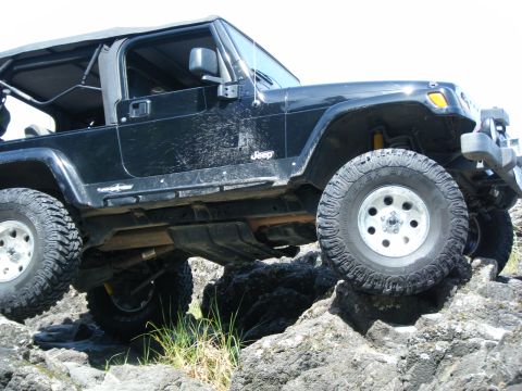 1994 Ford Explorer - A black Jeep Wrangler navigates a rocky terrain from the side.