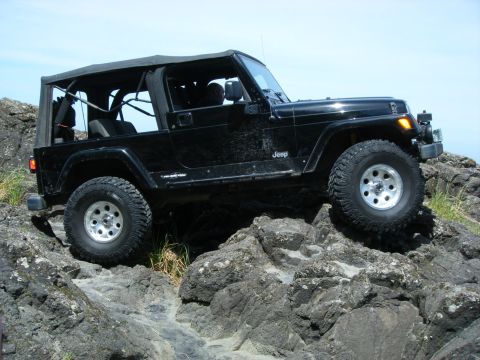 1994 Ford Explorer - A black Jeep Wrangler navigates a challenging rocky trail under a clear blue sky.