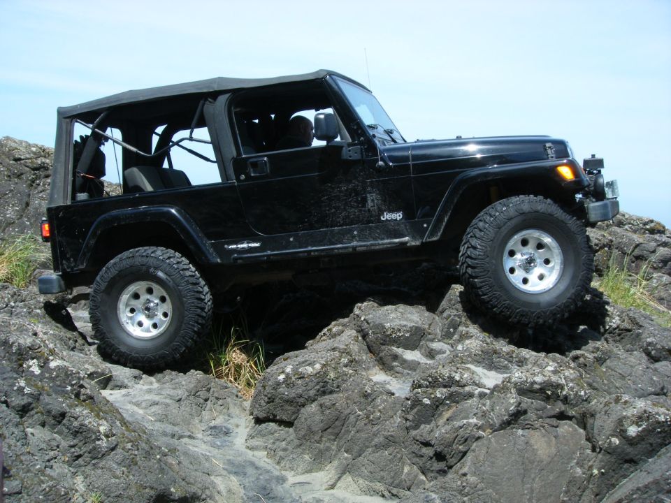 Black Jeep Wrangler driving over large rocks on a sunny day