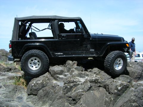 1994 Ford Explorer - A black Jeep Wrangler navigates a rocky coastal path under a clear blue sky.