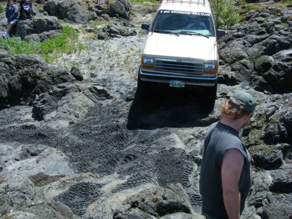 Tan 1990s Ford Explorer 4x4 on rocky terrain with tire tracks, person in foreground.