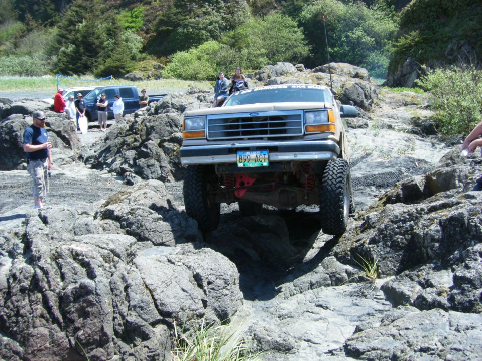 Tan 1990s Ford Explorer off-roading on a rocky beach.