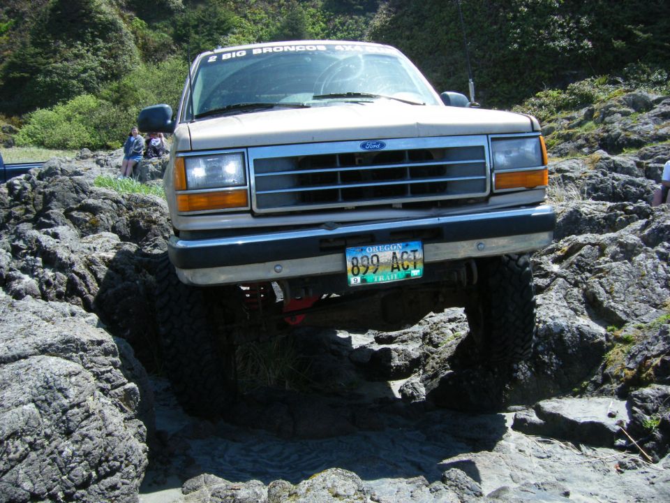 Tan 1990s Ford Explorer off-roading on rocks, close-up of front end.