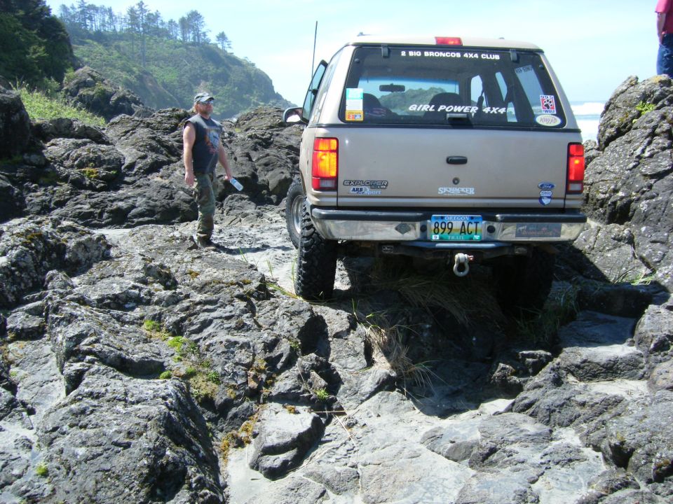 Tan 1994 Ford Explorer on a rocky coastal trail, rear view.