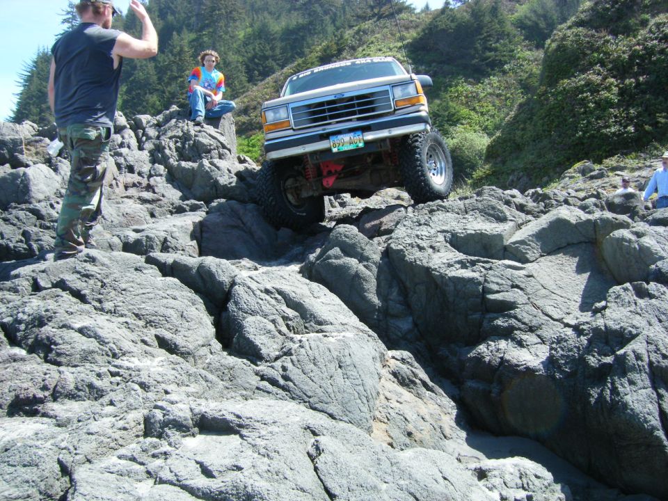 Lifted Ford Explorer driving over rocks on a coast.