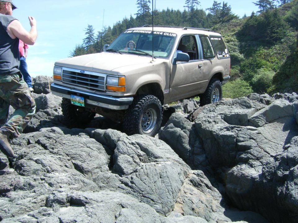 Tan Ford Explorer driving over rocks, with a person in camo pants nearby.