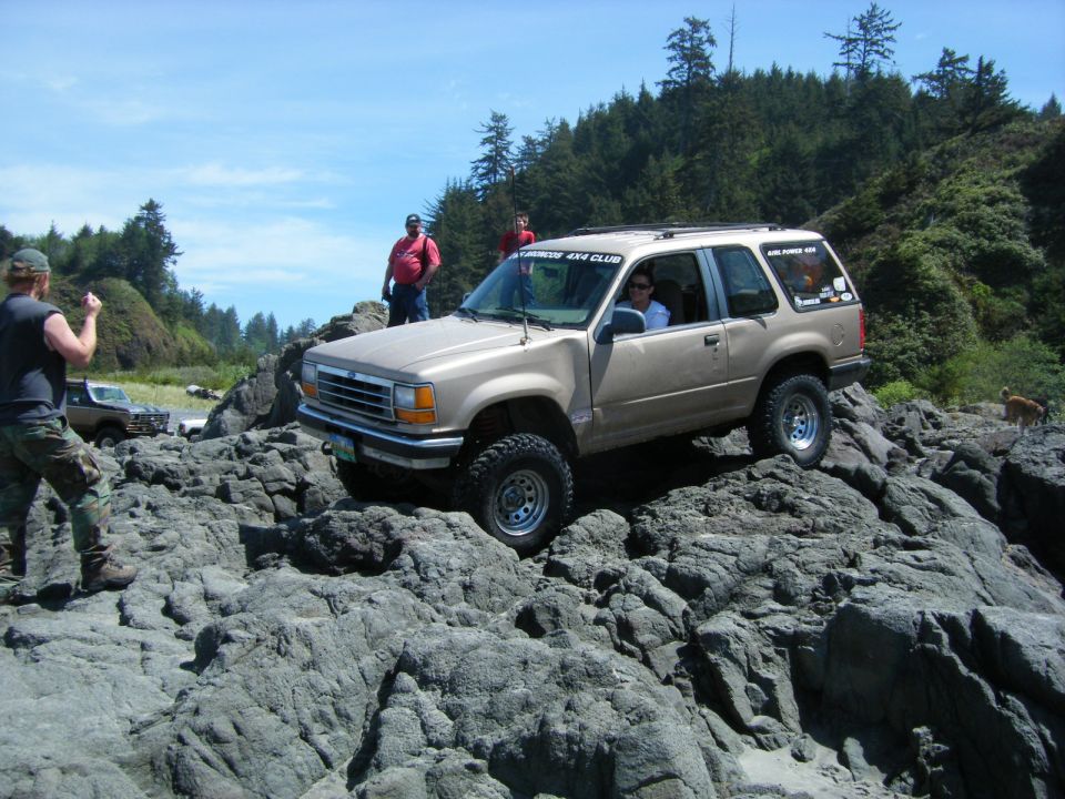 Tan 1990s Ford Explorer off-roading on rocks with two people.