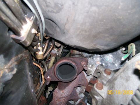 1995 Mercury Grand Marquis - Tight under-hood/underbody view of a rusty cast-iron exhaust manifold outlet flange with its two studs exposed after the downpipe was remov…