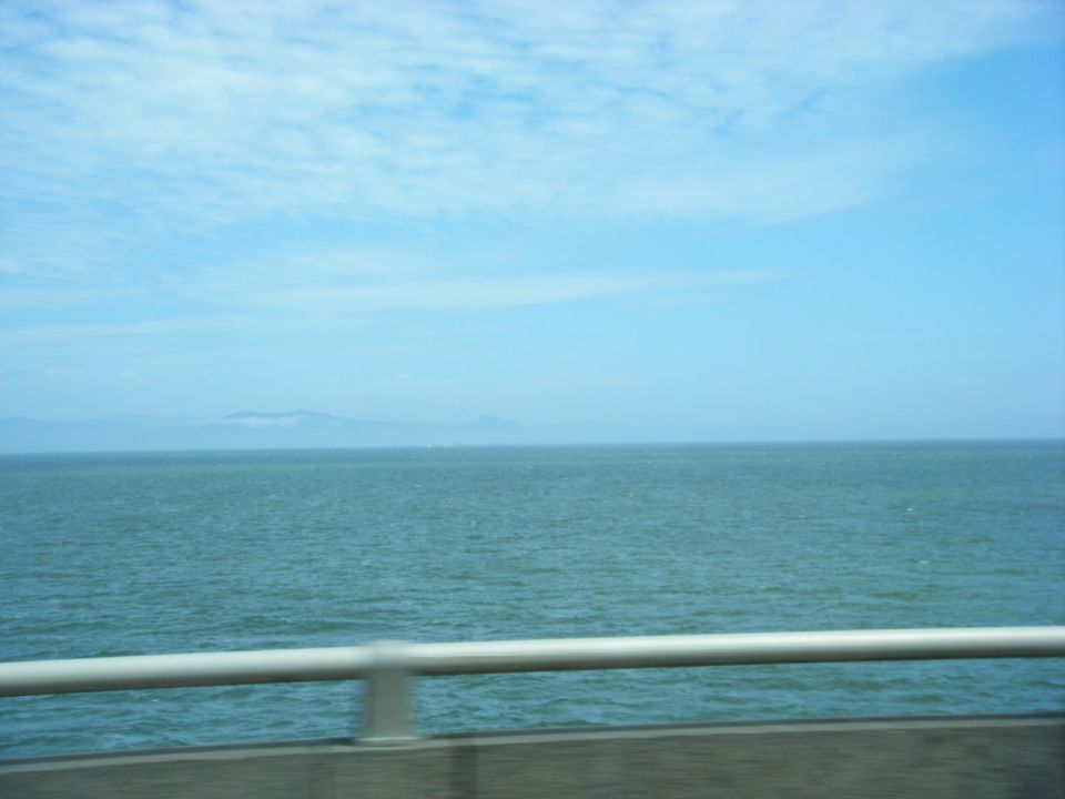 Ocean with a railing in the foreground and mountains in the distance.