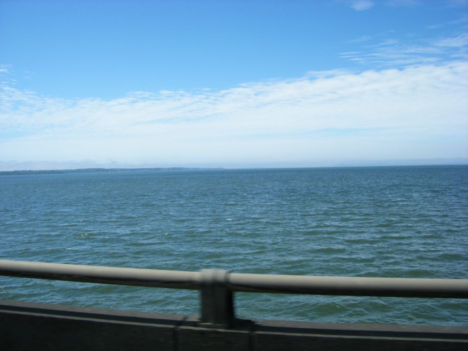 Water under a blue sky with a railing in the foreground.