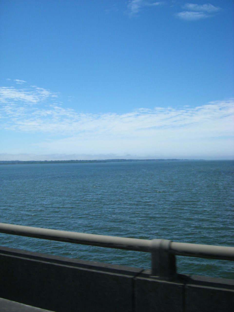 Calm water under a blue sky with clouds, viewed from a bridge railing.