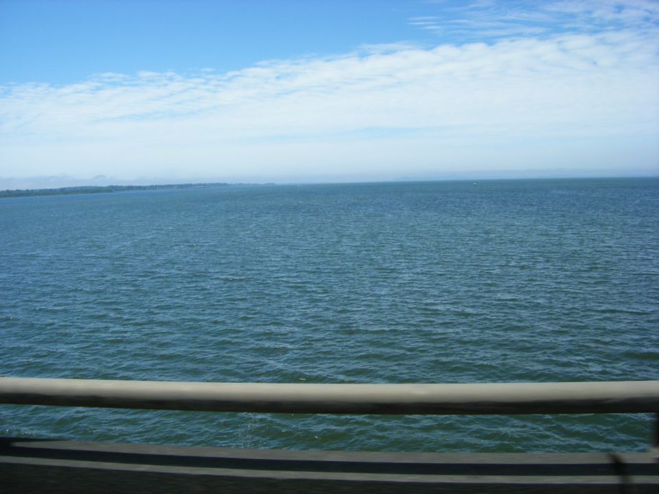 Calm blue water under a bright blue sky with scattered clouds. Railing in foreground.