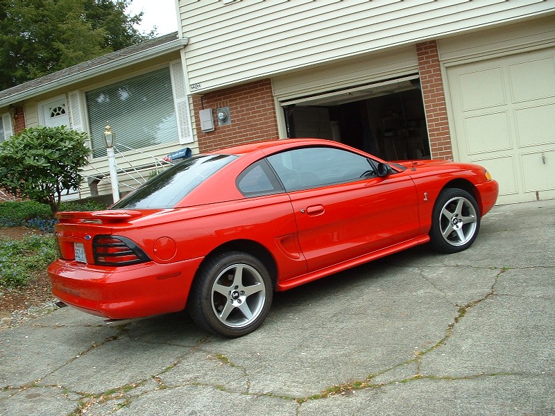 Red 1994 Ford Mustang coupe, rear three-quarter view, parked in driveway by garage