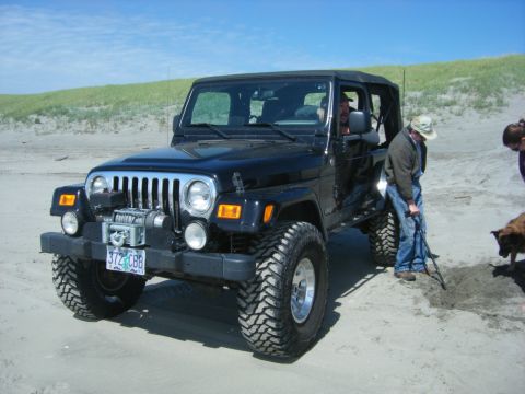 1994 Ford Explorer - A black Jeep Wrangler equipped with a winch and off-road tires is parked on a sandy beach under a clear blue sky.