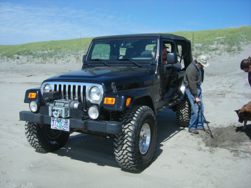 Black Jeep Wrangler with winch and off-road tires on a sandy beach