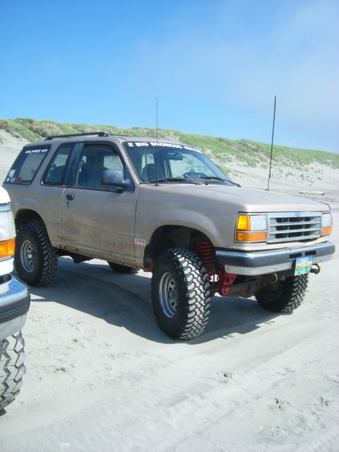 1994 Ford Explorer - A lifted 1994 Ford Explorer sits on a sandy beach under a clear blue sky, with dunes in the background.