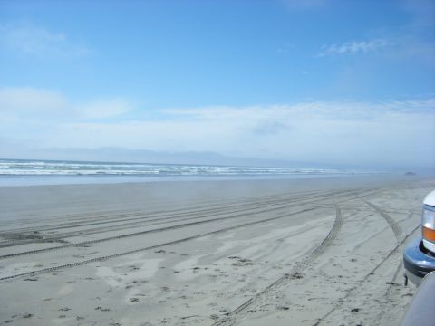 1994 Ford Explorer - Tire tracks mark the sand on a wide beach with the ocean in the background under a cloudy sky.