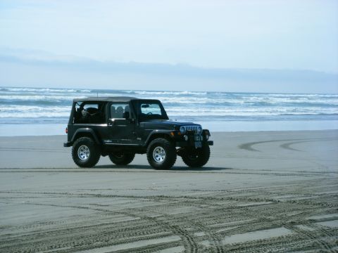 1994 Ford Explorer - A black Jeep Wrangler drives on the sand near the ocean, leaving tire tracks behind.
