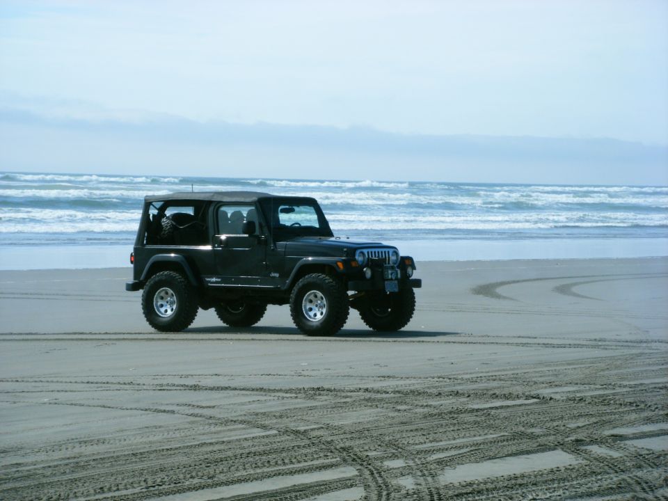 Black Jeep Wrangler parked on a sandy beach with ocean waves in the background