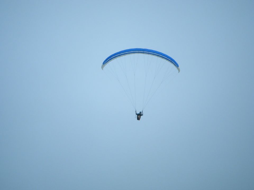 Paraglider with blue and white canopy against a pale blue sky