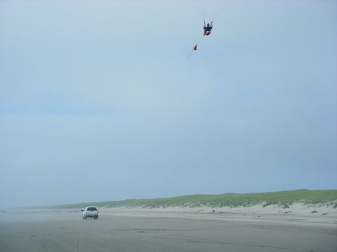 1994 Ford Explorer - A paraglider soars above a beach where a white SUV is driving along the shore.