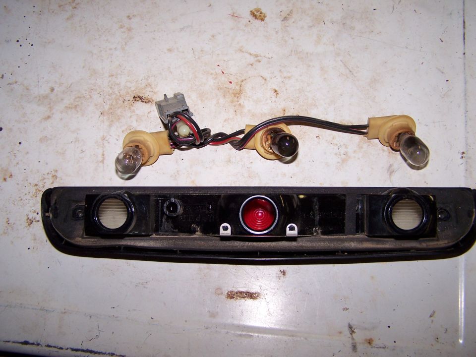 Disassembled brake light housing with three-bulb wiring pigtail on a workbench