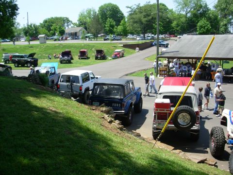 1983 Ford Bronco - Several classic Ford Broncos and other vehicles are gathered at an outdoor event, with people milling about.