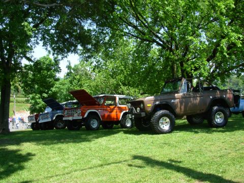 1983 Ford Bronco - Several Ford Broncos are lined up on a grassy field under trees.