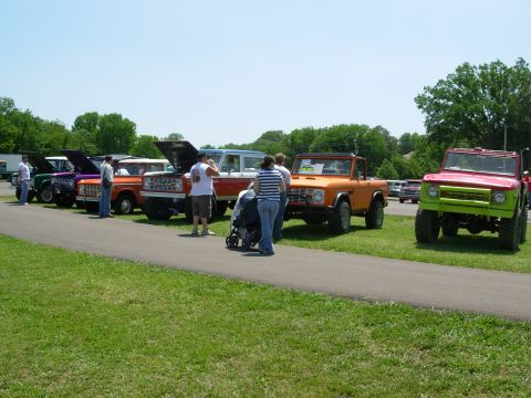 1983 Ford Bronco - A collection of Ford Broncos are displayed outdoors on a sunny day, with people milling around them.