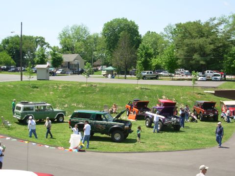 1983 Ford Bronco - A gathering of customized off-road vehicles displayed on a grassy field under a clear sky.