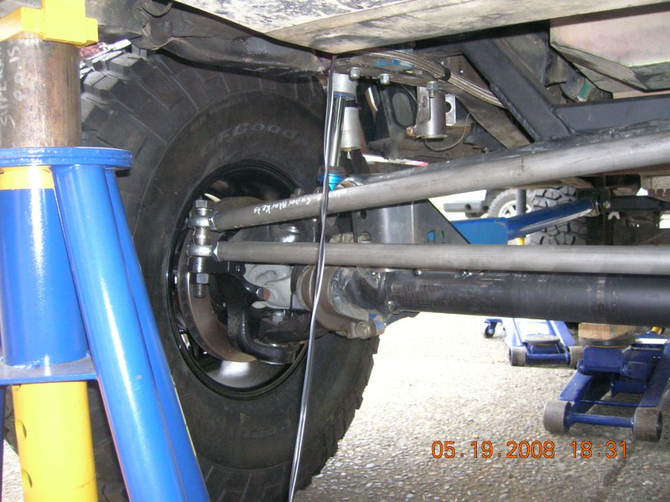 Close-up of modified suspension components and tire on a vehicle, with other vehicles and jacks visible in the background