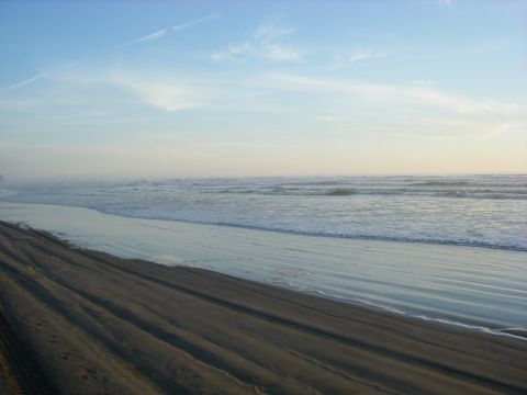 1994 Ford Explorer - Tire tracks mark the sand on a beach with ocean waves under a hazy sky.
