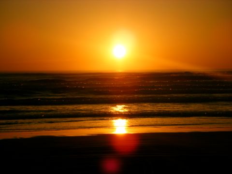 1994 Ford Explorer - The sun dips below the horizon, casting a warm orange glow over the ocean waves and sandy beach.