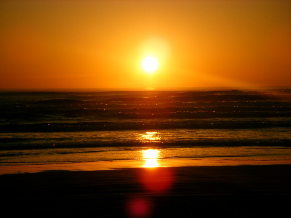 Sun setting over the ocean with waves crashing on the shore