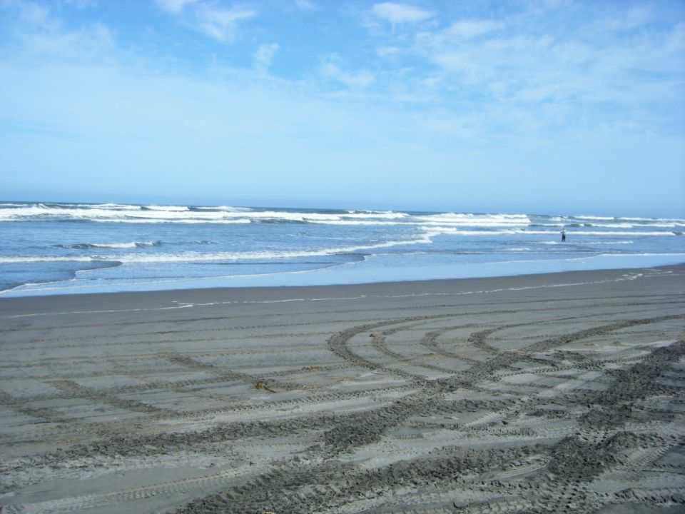 Tire tracks on a sandy beach with waves in the background