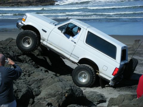 1994 Ford Explorer - A white SUV navigates a rocky shoreline with waves crashing in the background.