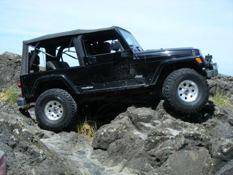 1994 Ford Explorer - A black Jeep Wrangler navigates a rocky terrain under a clear blue sky.