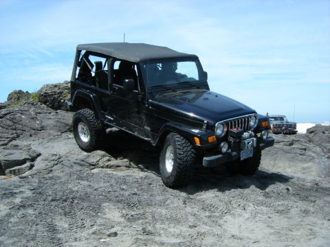 1994 Ford Explorer - A black Jeep Wrangler is parked on a rocky beach with another vehicle in the background.
