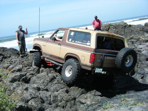 1994 Ford Explorer - Ford Bronco tackles challenging rocky coastal terrain with ocean waves in the background.
