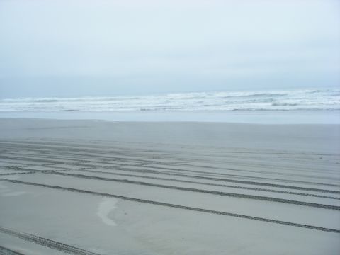 1994 Ford Explorer - Tire tracks mark the sand on a beach, leading towards the ocean under an overcast sky.