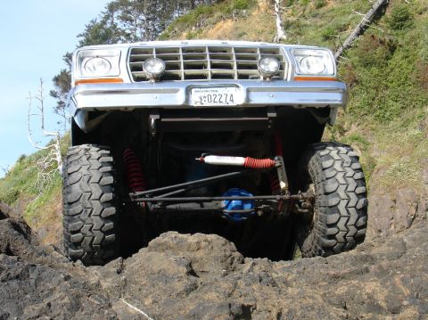 1978 Ford Bronco - A white 1978 Ford Bronco navigates rocky terrain with its lifted suspension and large off-road tires.