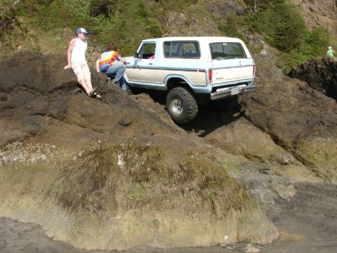 1978 Ford Bronco - A 1978 Ford Bronco navigates a rocky coastal terrain, with two individuals observing the off-road adventure.