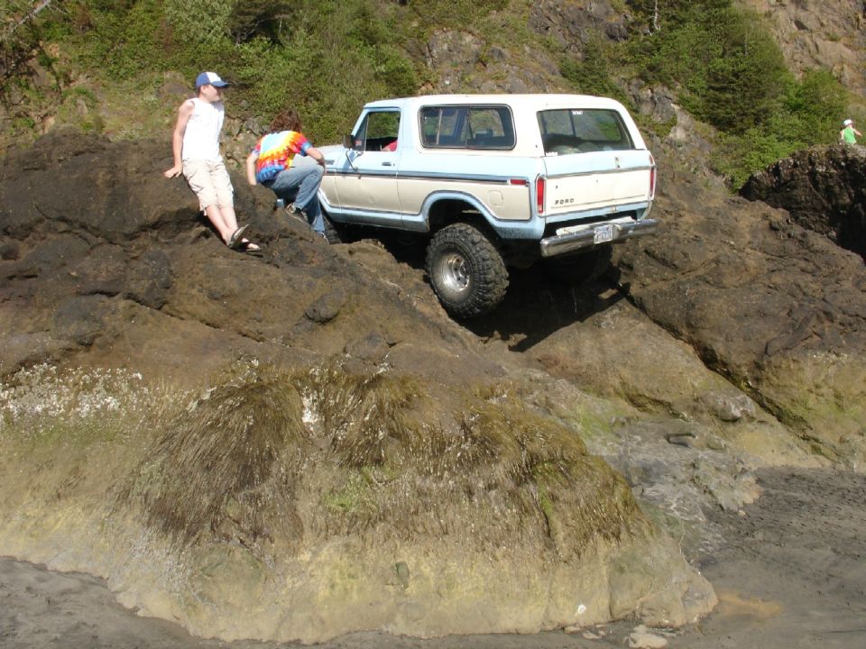 1978 Ford Bronco climbing over large rocks near a beach