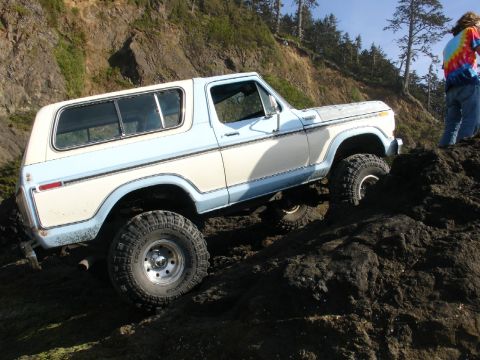 1978 Ford Bronco - A two-tone 1978 Ford Bronco navigates a challenging rocky incline near the coast.