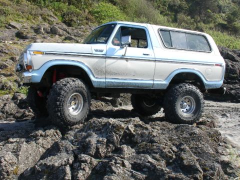 1978 Ford Bronco - A 1978 Ford Bronco navigates a rocky beach with its suspension and tires clearly visible.